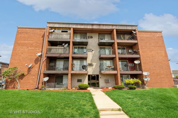 Front view of a four-story apartment building with balconies and brick construction.
