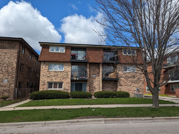 Front view of a three-story brick apartment building with balconies.