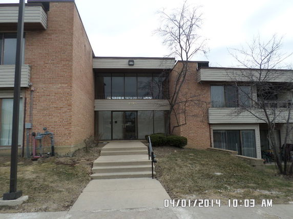 Front view of a multi-story brick building with a central entrance and steps leading to the door.