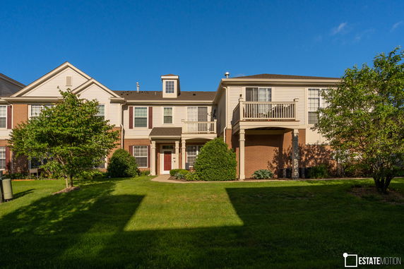 Front view of a two-story house with a small balcony and red shutters.