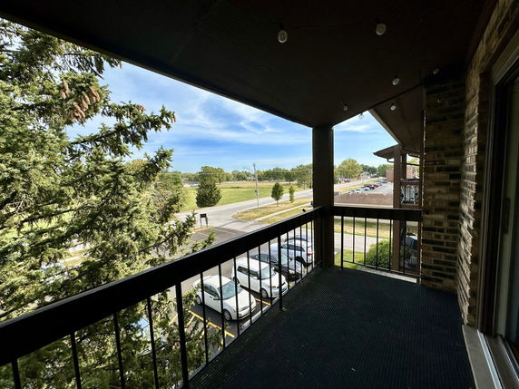 Balcony view overlooking a grassy area and parking lot, with trees and clear sky in the background.