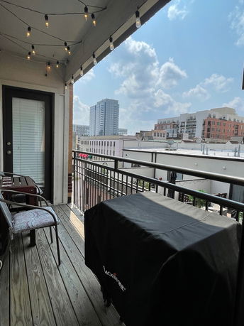 View of surrounding buildings from a balcony with string lights and outdoor furniture.