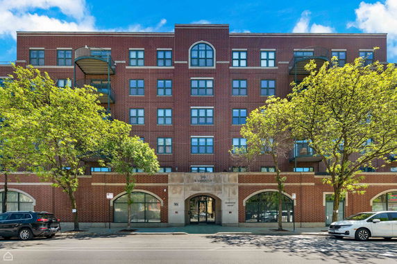 Front view of a multi-story brick building with balconies and large arched windows.
