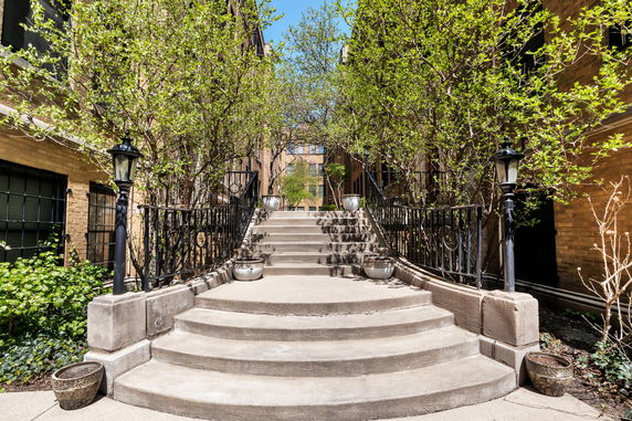 Front view of a building with steps leading up to an entrance flanked by railings and plants.