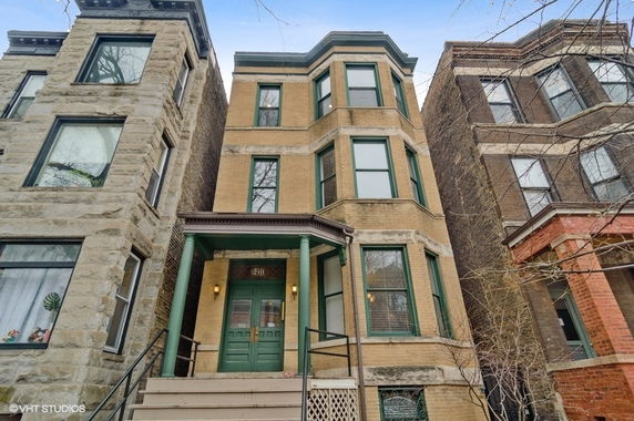 Front view of a three-story brick building with bay windows and a green porch entrance.