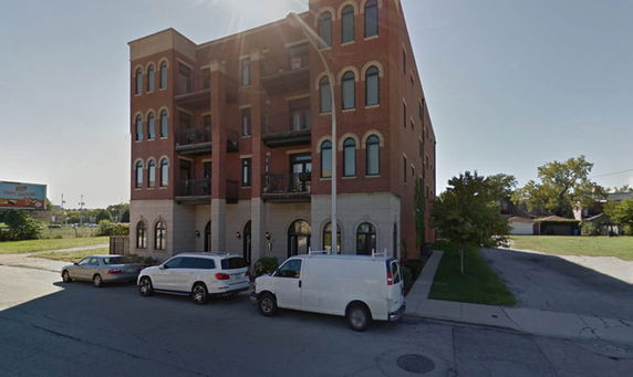 Front view of a multi-story brick building with arched windows and parked vehicles outside.