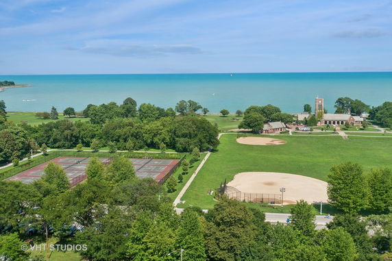 Panoramic view of a coastal park with tennis courts, a baseball field, and a building near the shore.
