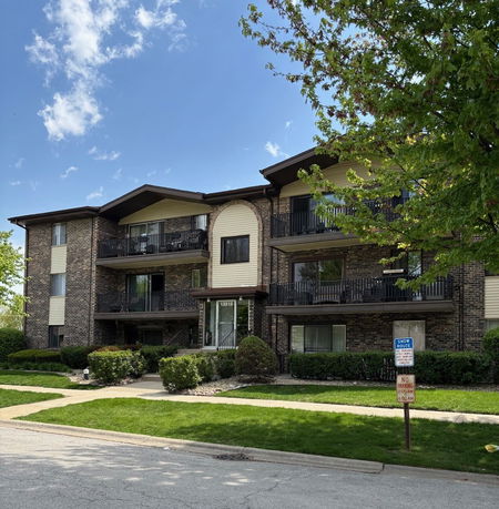 Front view of a multi-story apartment building with balconies and brick facade.