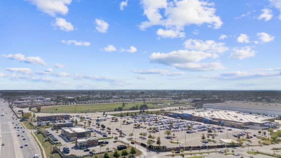 Panoramic view of a vast outdoor area including a large parking lot, several buildings, and wide open spaces under a blue sky with scattered clouds.
