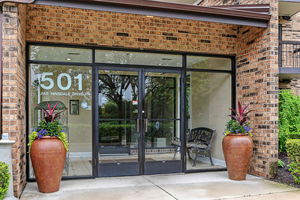 Front view of a brick building entrance with large glass doors and potted plants.