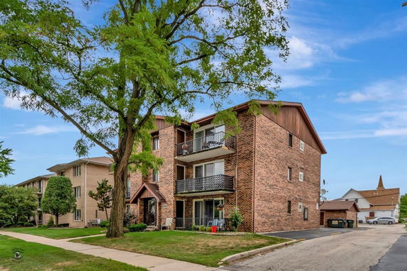 Front view of a three-story brick apartment building with balconies.