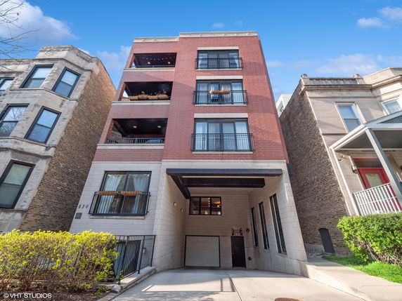 Front view of a multi-story apartment building with balconies and brick facade.