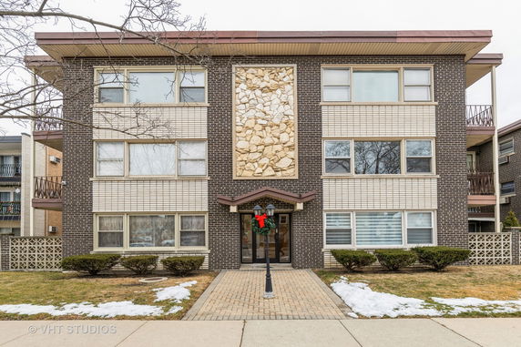Front view of a three-story brick apartment building with a distinctive stone feature and entryway.