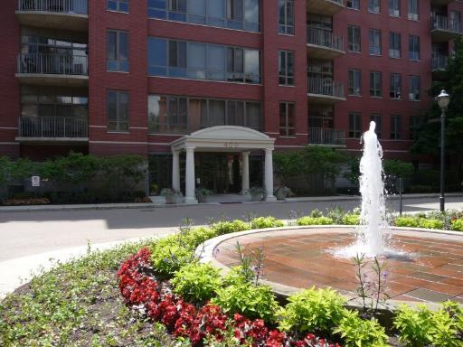 Front view of a multi-story brick building with balconies and a fountain in the foreground.