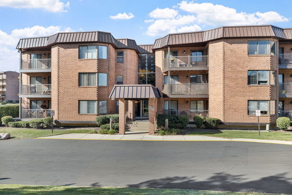 Front view of a three-story brick apartment building with balconies and an entrance canopy.
