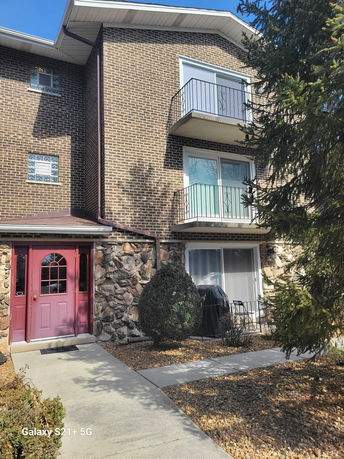 Front view of a multi-story brick building with balconies and a red entrance door.