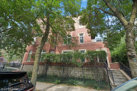 Front view of a multi-story brick building with gated entrance and stairs.