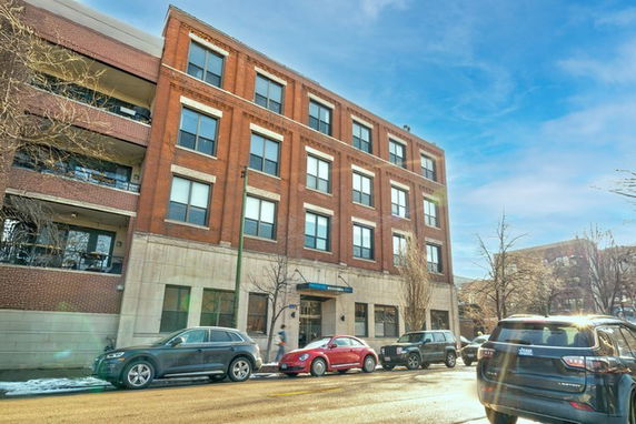 Front view of a four-story brick building with large windows and a ground-level entrance.