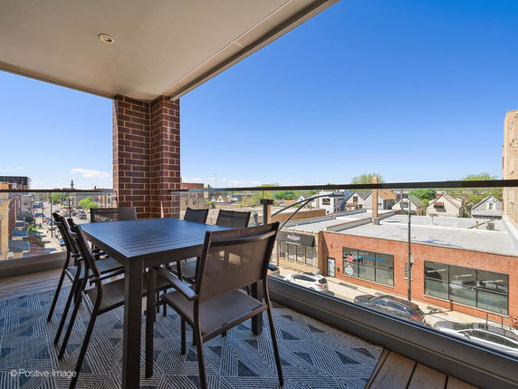 Outdoor seating area on a balcony with a panoramic view of a street and nearby buildings.