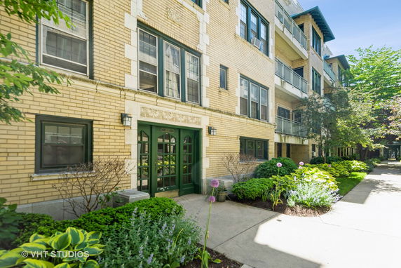 Front view of a multi-story brick apartment building with green doors and windows.