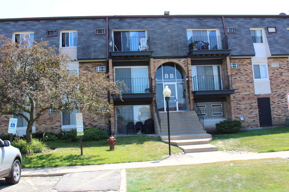 Front view of a three-story apartment building with balconies and a central entrance marked 8B.