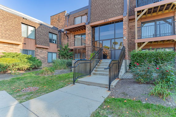 Front view of a multi-story brick building with balconies and a central entrance with stairs.