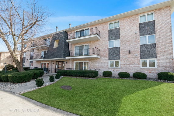 Front view of a three-story brick apartment building with balconies.