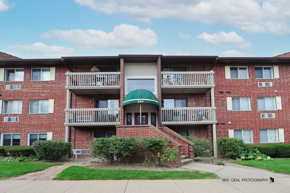 Front view of a multi-story brick apartment building with balconies and a green awning over the entrance.