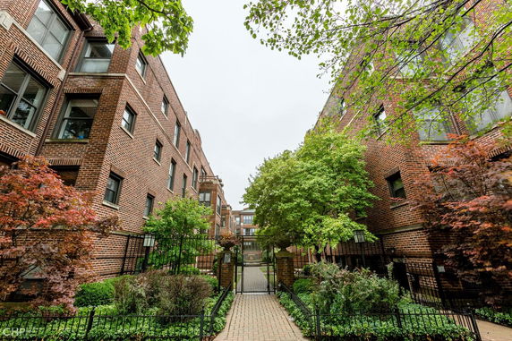 View of a brick apartment building with multiple windows and greenery.
