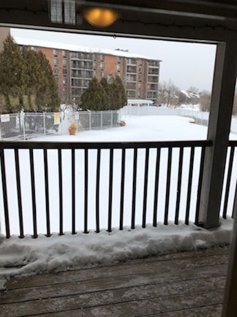 Panoramic view of a snowy area with a building in the background seen from a balcony.