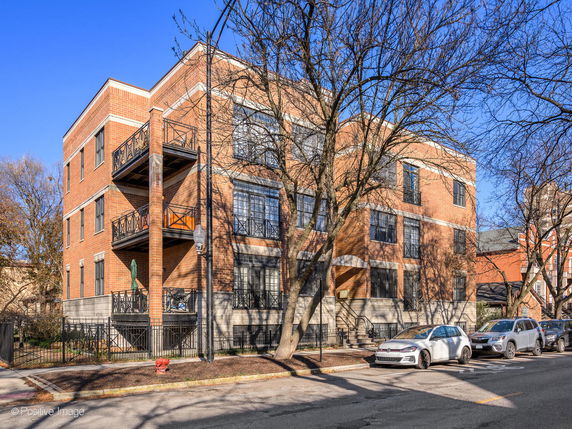 Front view of a multi-story brick building with balconies and a fenced entrance.