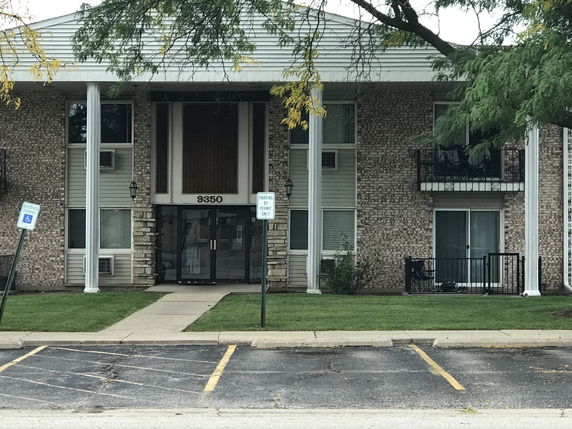Front view of a multi-story building with balconies and a parking area.