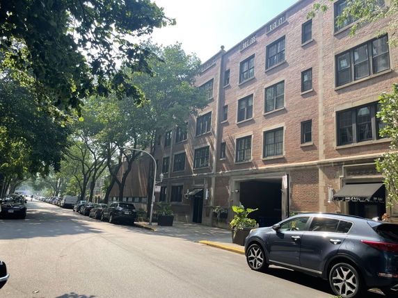 Front view of a multi-story brick building along a street with cars parked on either side.