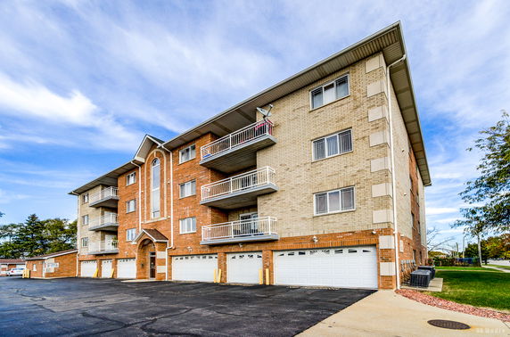 Front view of a multi-story apartment building with balconies and multiple garage doors.