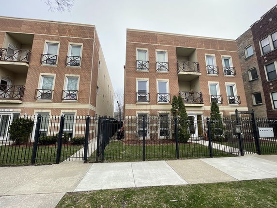 Front view of a three-story brick apartment building with balconies.