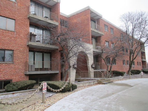 Front view of a three-story brick apartment building with balconies and a main entrance.
