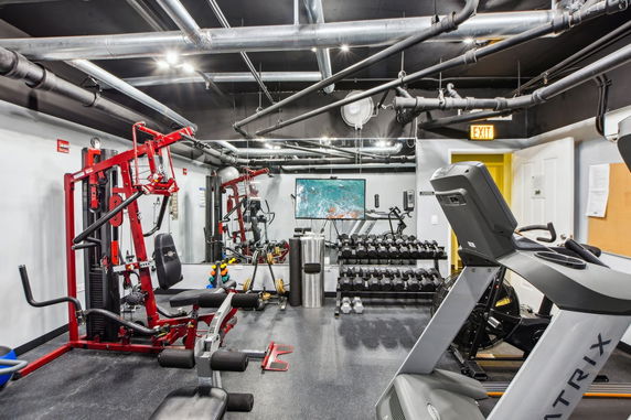 Indoor gym area with various exercise equipment including a treadmill, weight machines, and dumbbells.
