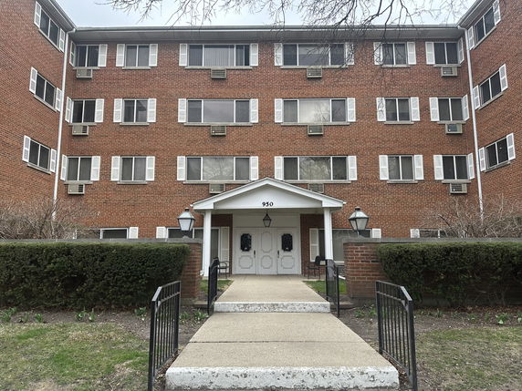 Front view of a multi-story brick building with white window shutters and a central entrance.