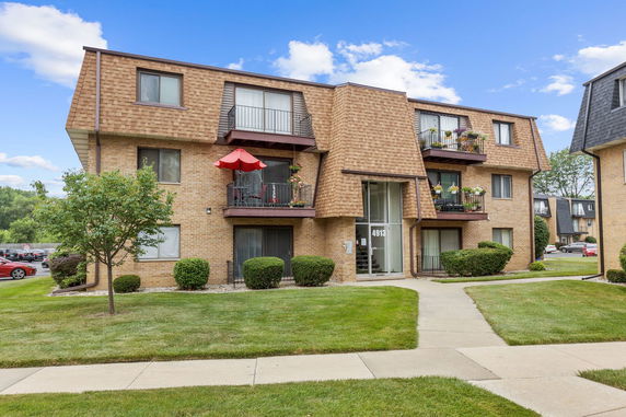 Front view of a multi-story apartment building with balconies and a red umbrella.