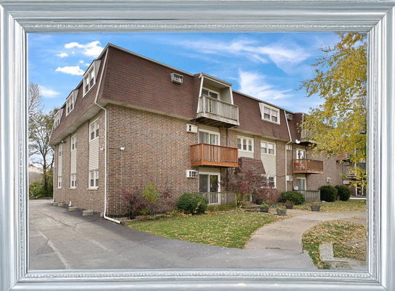 Front view of a multi-story brick building with balconies and a sloped roof.