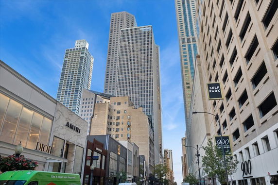 Front view of tall urban buildings and a parking structure on a city street.