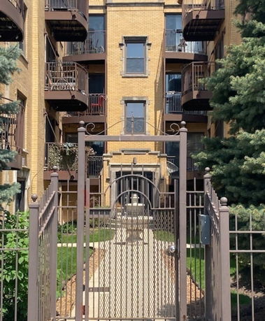 Front view of a multi-story brick building with balconies and a gated entrance.