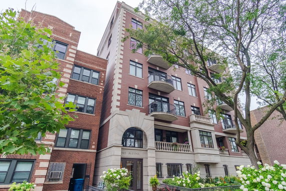 Front view of a multi-story apartment building with balconies and a decorated entrance.