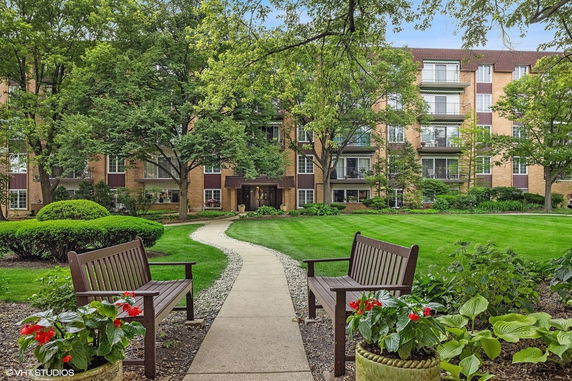 Front view of a multi-story apartment building with balconies and a pathway leading through a garden.