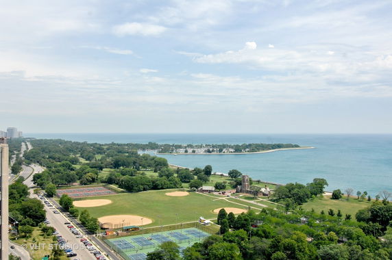 Wide-angle view of a coastal area with greenery, roads, sports fields, and water.