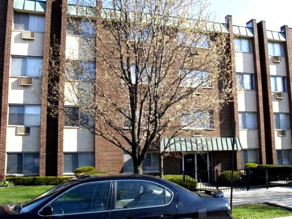 Front view of a multistory brick building with multiple windows and a tree in front.