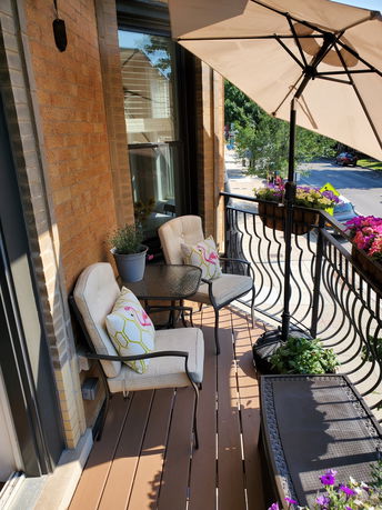 A balcony with chairs, umbrella, and potted plants overlooking a street.