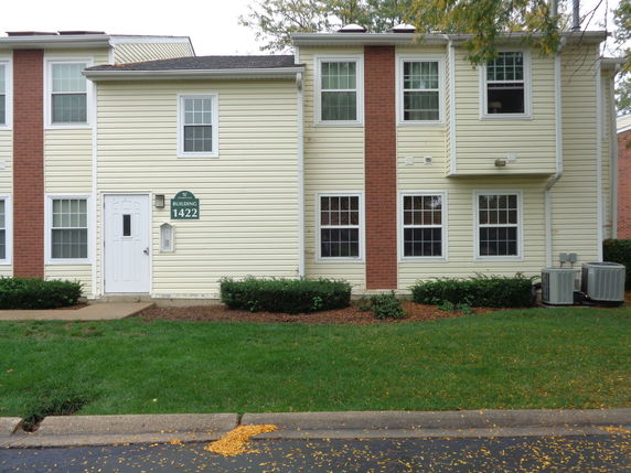 Front view of a two-story residential building with beige siding and brick accents.