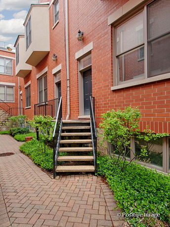 Front view of a multi-story brick townhouse with stairs leading to the entrance.