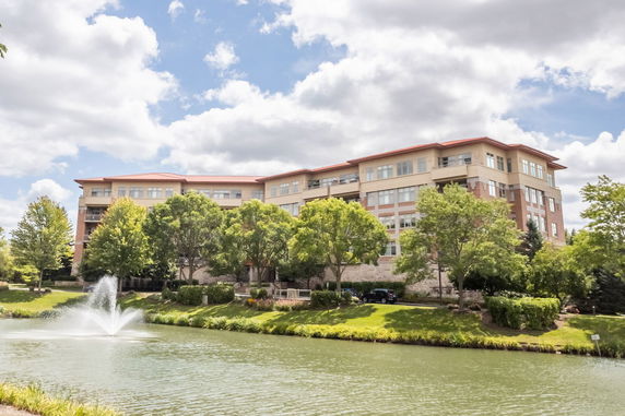Front view of a multi-story residential building with trees and a pond.